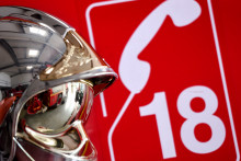 Casque de pompiers sur fond rouge, affichant le numéro de téléphone à composer pour les joindre, le 18 (photo d'illustration)