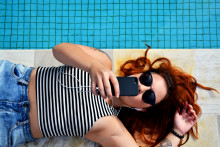 Une femme avec son smartphone au bord de la piscine (illustration).