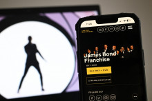 Le site des studios MGM affiche les détails de la franchise James Bond sur l'écran d'un téléphone, à côté d'une photographie affichée sur l'écran d'un ordinateur portable.
