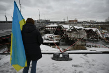 Une femme brandissant un drapeau ukrainien se tient sur un pont détruit à Irpin, au nord-ouest de Kiev, lors d'une cérémonie commémorative le 24 février 2026, à l'occasion du quatrième anniversaire de l'invasion de l'Ukraine par la Russie.