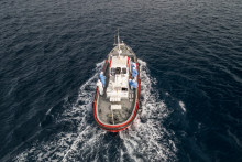 Des membres d'équipage portant des combinaisons de protection à bord d'un bateau se dirigeant vers le port depuis le navire de croisière MV Hondius
