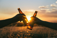 Deux personnes qui trinquent avec des bières devant le coucher du soleil. (Illustration)