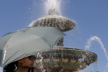Une femme se protège du soleil avec un parapluie près de l'une des fontaines de la place de la Concorde, à Paris le 27 mai 2026.