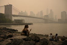 Des passants sont assis près du pont de Brooklyn alors que la fumée des feux de forêt provenant du Canada provoque un brouillard de fumée, le 16 juillet 2026 à New York.