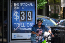 Un cycliste s'arrête devant une affiche montrant la dette nationale américaine à Washington, D.C., le 19 août 2026.