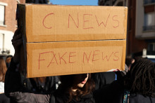 Le 8 octobre 2026, à Paris, un manifestant brandit un carton où l'on peut lire « CNEWS fake news », en référence à la chaîne de télévision française CNEWS,.