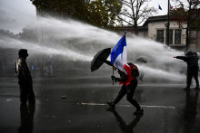 Un manifestant brandit le drapeau français et se protège d'un canon à eau lors d'une manifestation à Paris le 24 octobre 2026