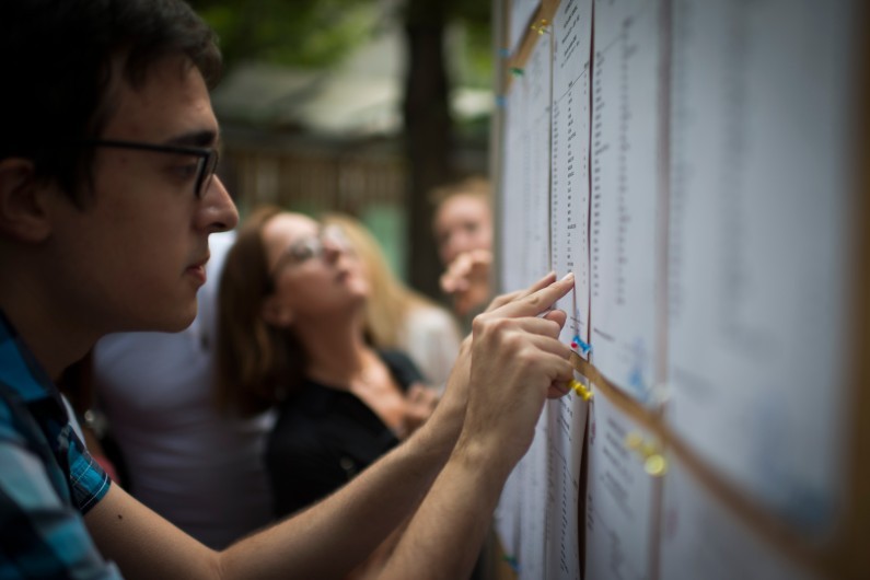 Des étudiants cherchent leurs noms sur le tableau des résultats du BAC d'un lycée