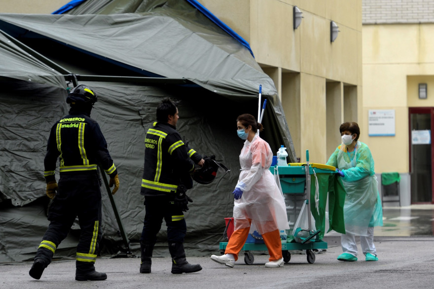 Le personnel de nettoyage portant des masques protecteurs et des pompiers passent devant un hôpital de campagne installé devant l'hôpital Gregorio Maranon de Madrid le 1er avril 2020.