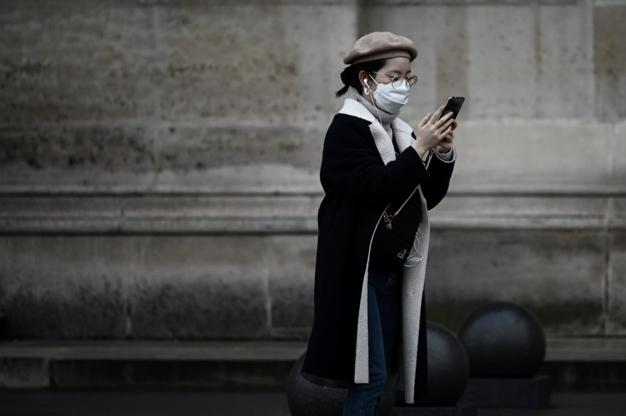 Une femme portant un masque marche dans la rue, avec un téléphone portable (illustration)