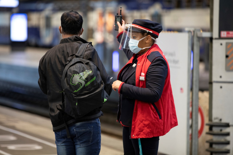 Une femme agent SNCF, portant un masque, et indiquant le chemin à un voyageur. (illustration)