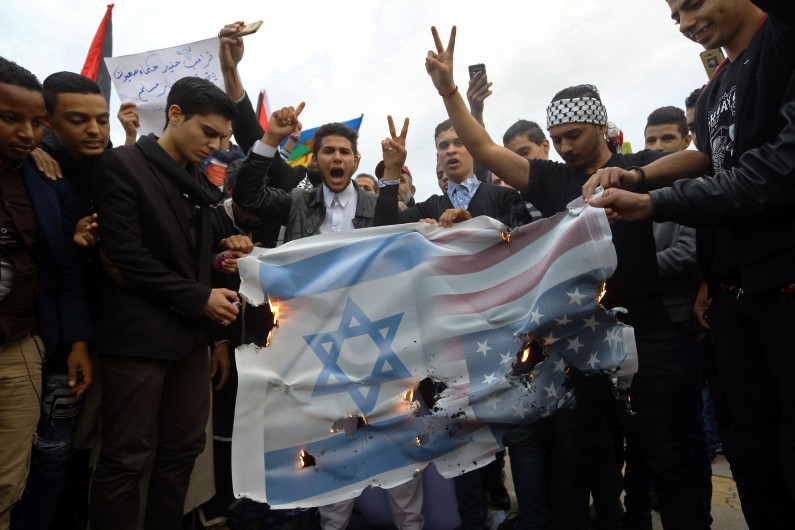 Des manifestants libyens et palestiniens brûlent une banderole portant le drapeau américain et israélien lors d'une manifestation, place des Martyrs à Tripoli le 8 décembre 2017.