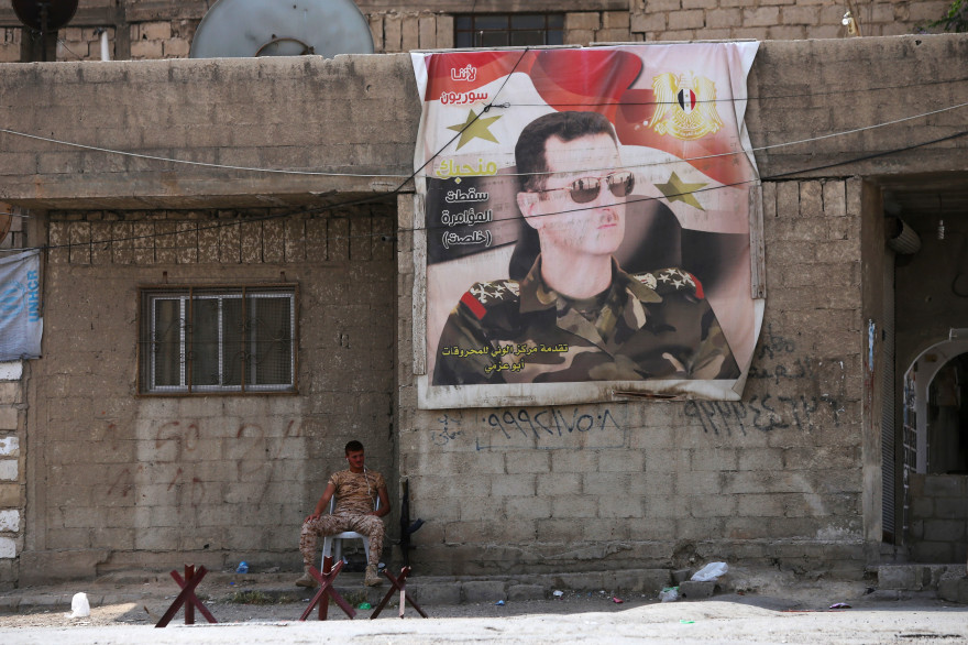 Un soldat syrien se tient devant un portrait de Bachar al-Assad en attendant les bus transportant les rebelles de la Ghouta, le 12 avril 2018