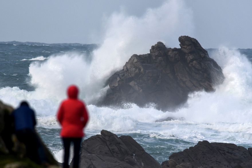Des passants regardent les hautes vagues s'écraser à Porspoder, dans l'ouest de la France le 27 décembre 2020, alors que la tempête Bella frappe la côte bretonne.